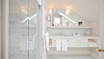 A modern bathroom with a glass shower enclosure, a white vanity with a mirror, and a marble-tiled floor.