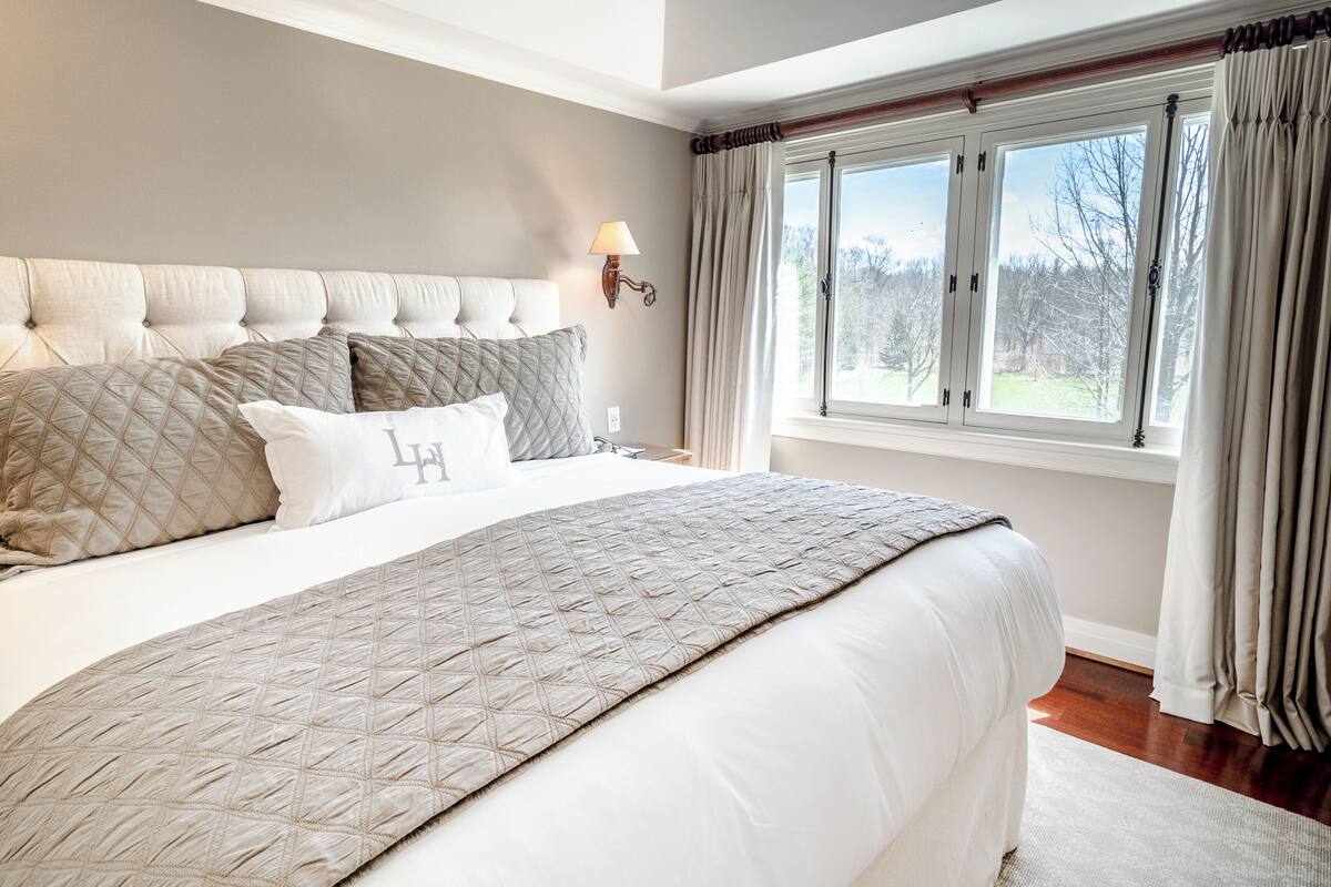 A bedroom with a large bed, a headboard, a nightstand, a lamp, and a window with curtains.