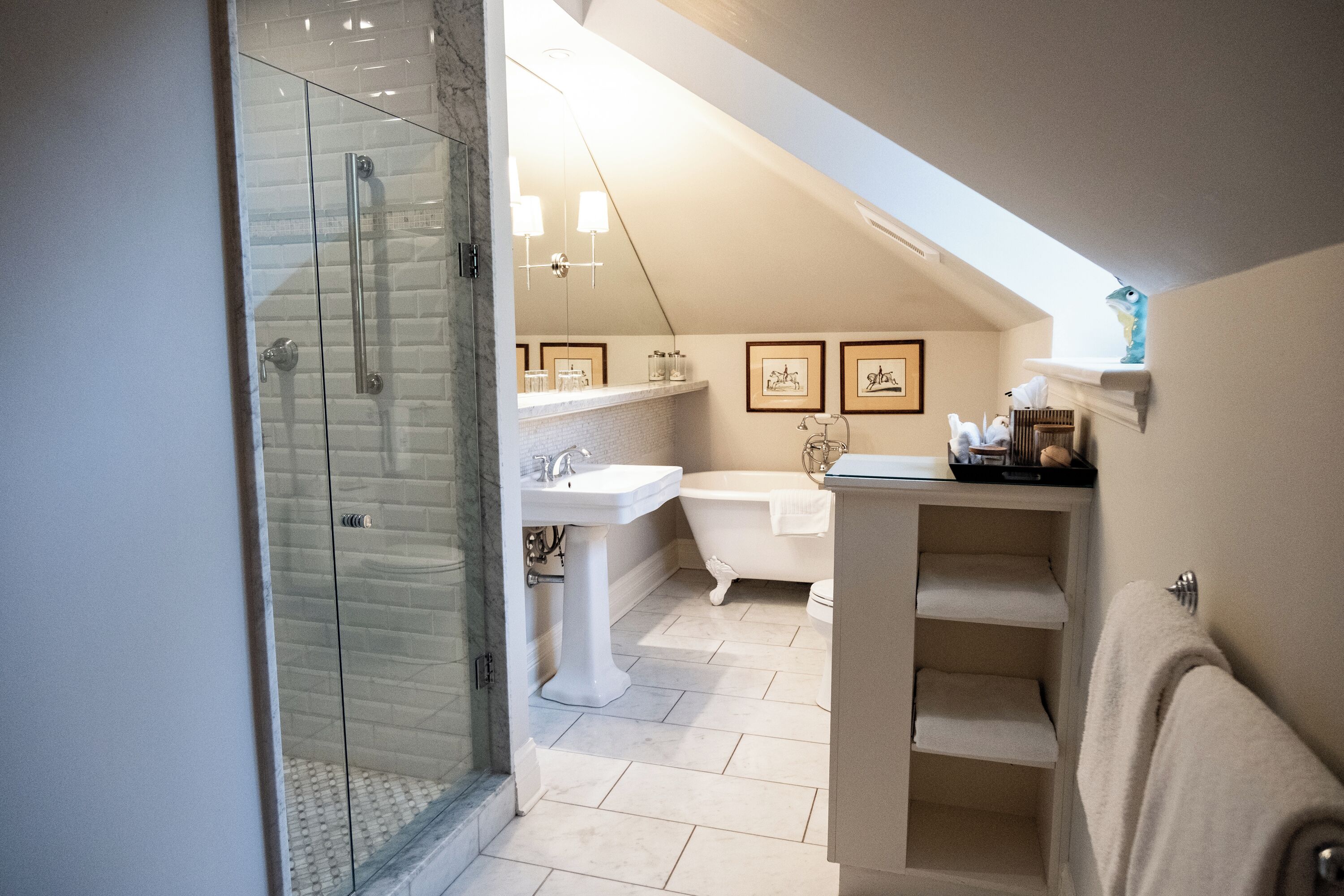 A bathroom with a glass shower enclosure, a pedestal sink, a freestanding bathtub, and a vanity with a towel rack.