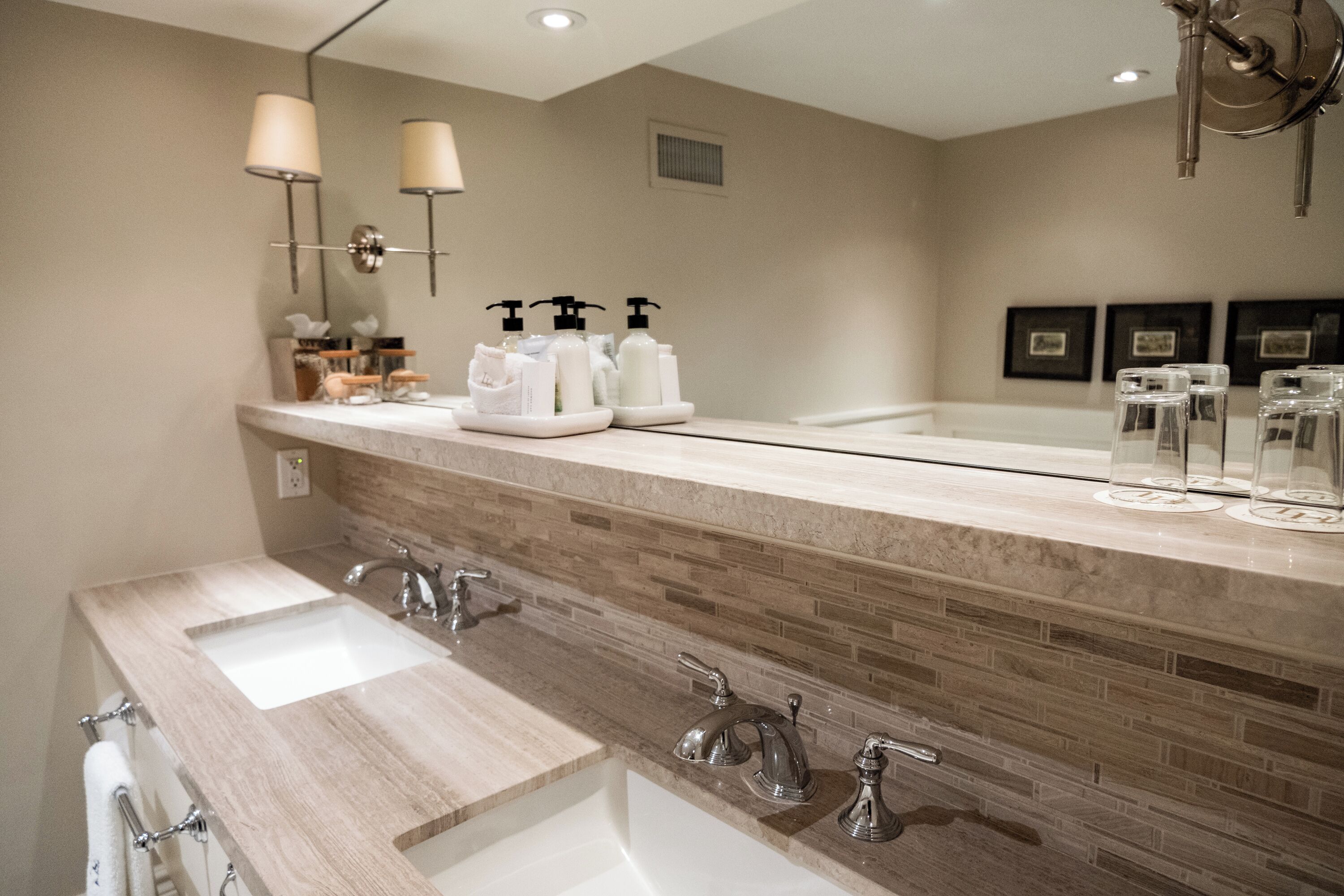 Un baño moderno con un espejo grande, tres lavamanos y un mueble de tocador con artículos de aseo.