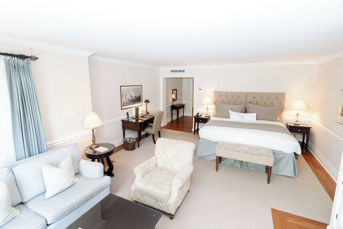 A hotel room with a large bed, a sofa, a chair, a desk, and two bedside tables with lamps.
