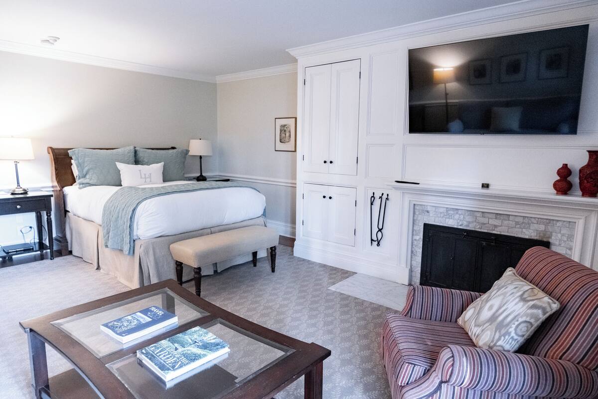 A bedroom with a bed, bedside tables, a TV, a fireplace, and a seating area with a sofa and a coffee table.