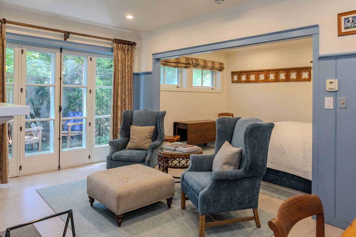 A bedroom with a large bed, two armchairs, a small table, and a window with curtains.