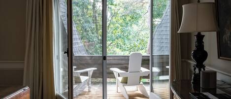 A room with a sliding glass door leading to an outdoor deck with two white chairs and a table.