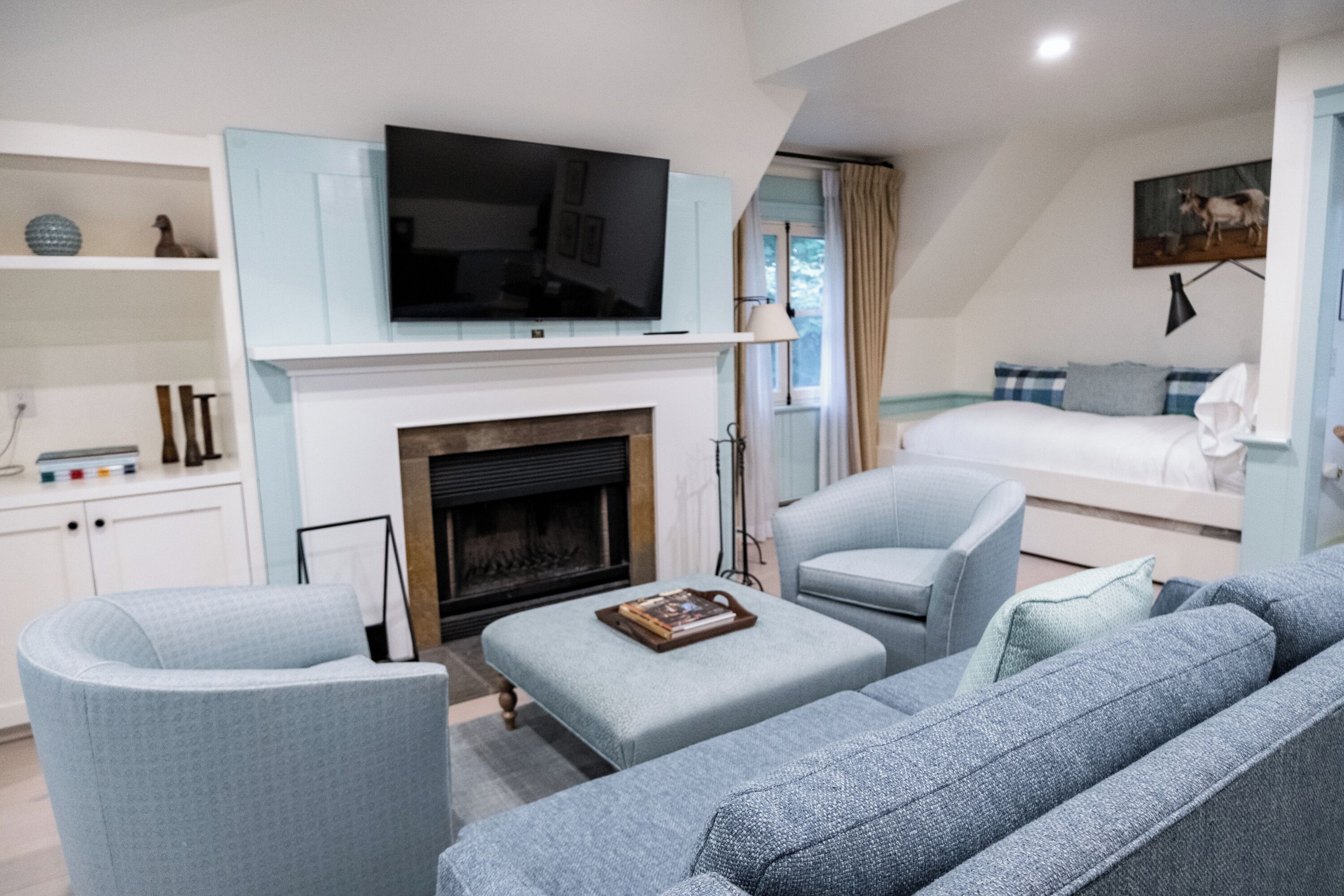 Una sala moderna con chimenea, televisor montado encima y una cama al fondo.