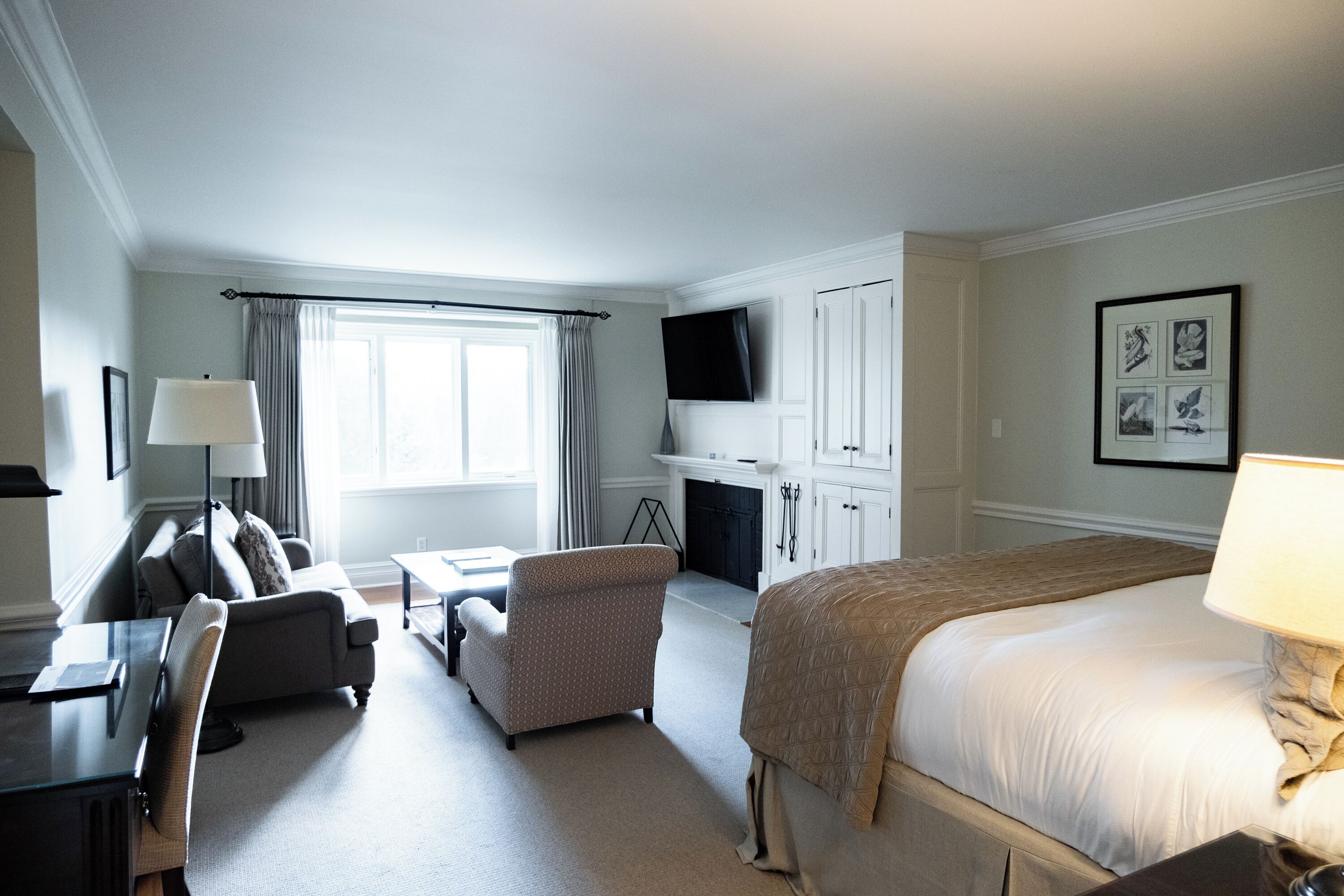 A hotel room with a bed, a desk, a chair, a TV, and a fireplace.