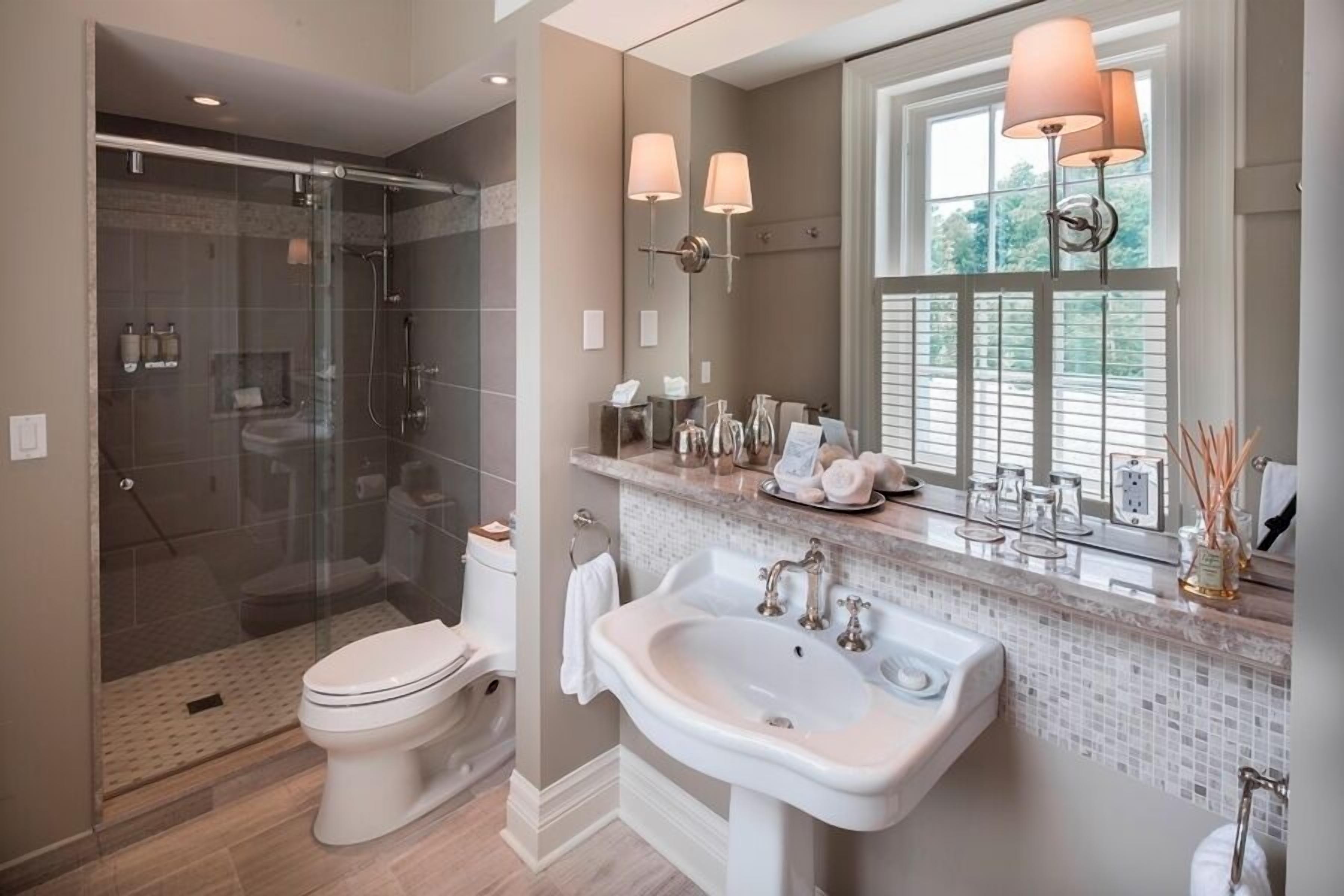 A modern bathroom with a glass-enclosed shower, a white toilet, and a large sink with a mirror above it.