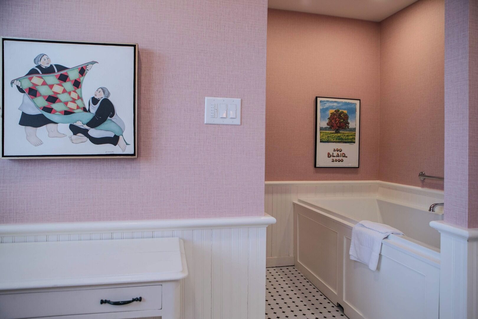 A bathroom with a white vanity, a bathtub, and two framed pictures on the wall.