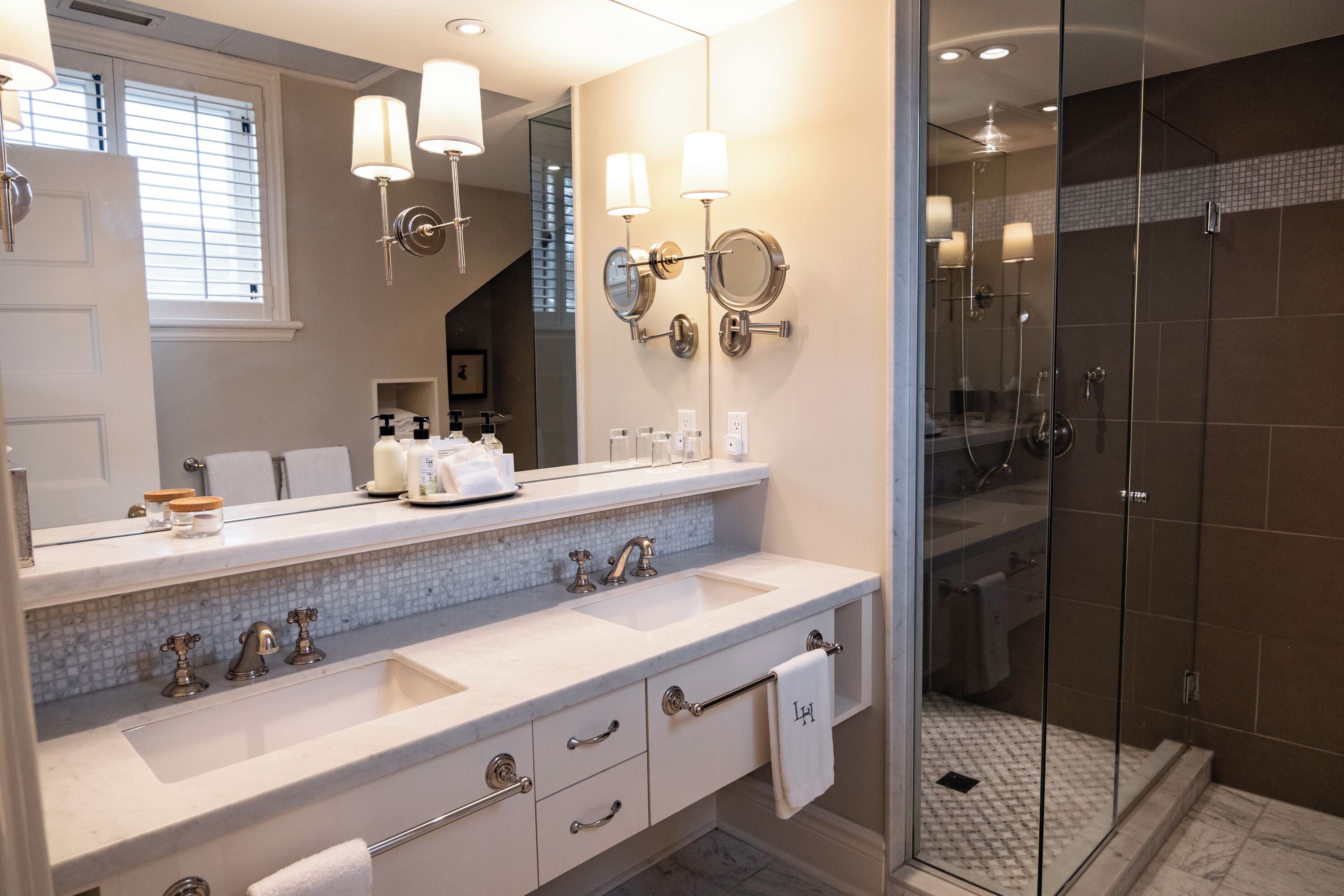 Un baño moderno con dos lavabos, un espejo grande y una ducha con mampara de vidrio.