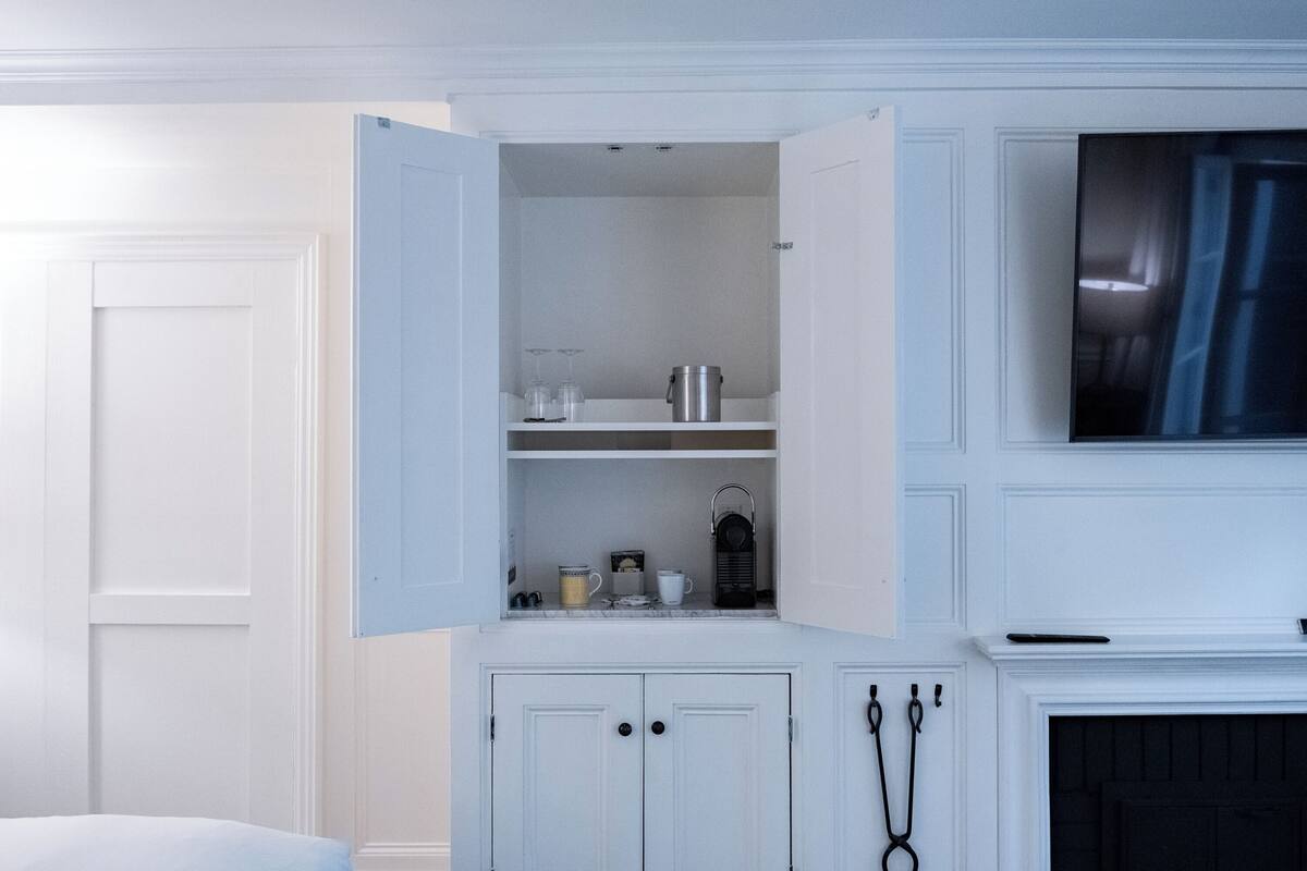 A room with a white door, a white cabinet with open shelves, and a fireplace.