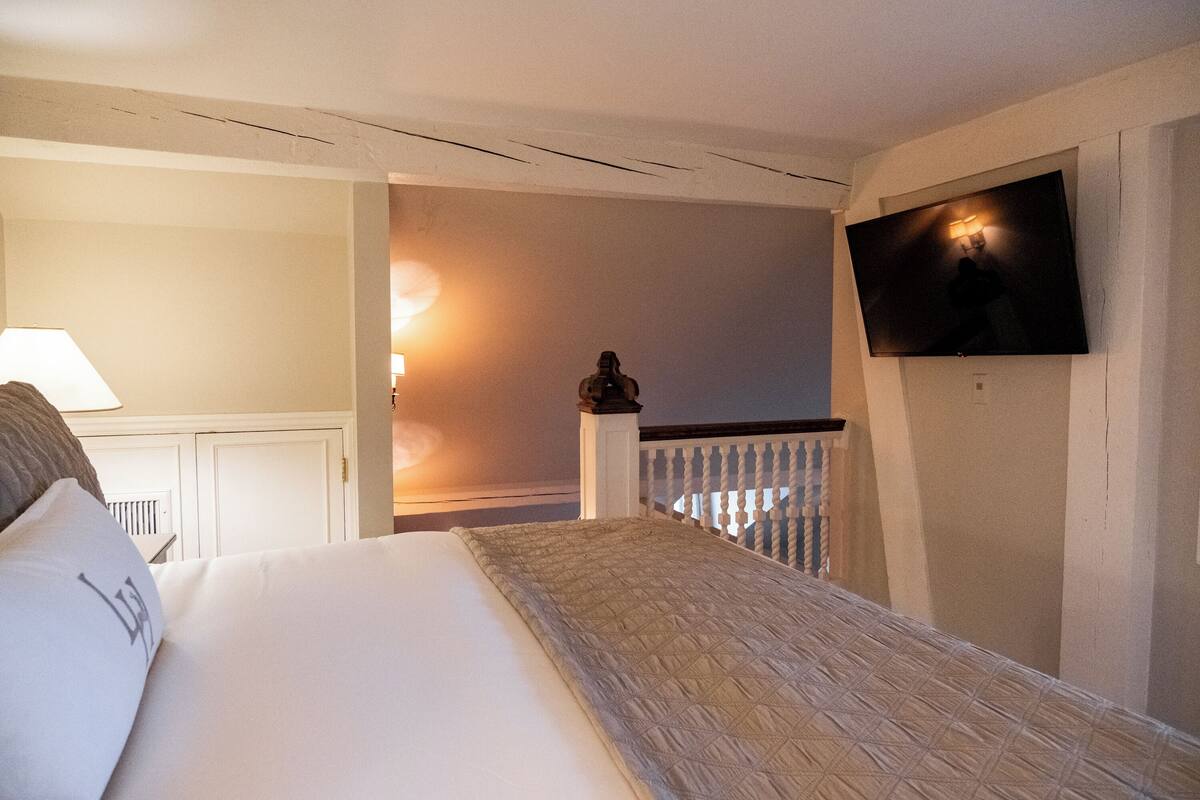 A bedroom with a bed, a TV mounted on the wall, a nightstand, and a lamp.