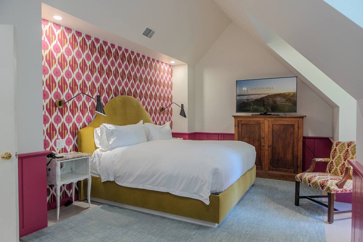 A bedroom with a bed, a television, a nightstand, a chair, and a patterned wall.