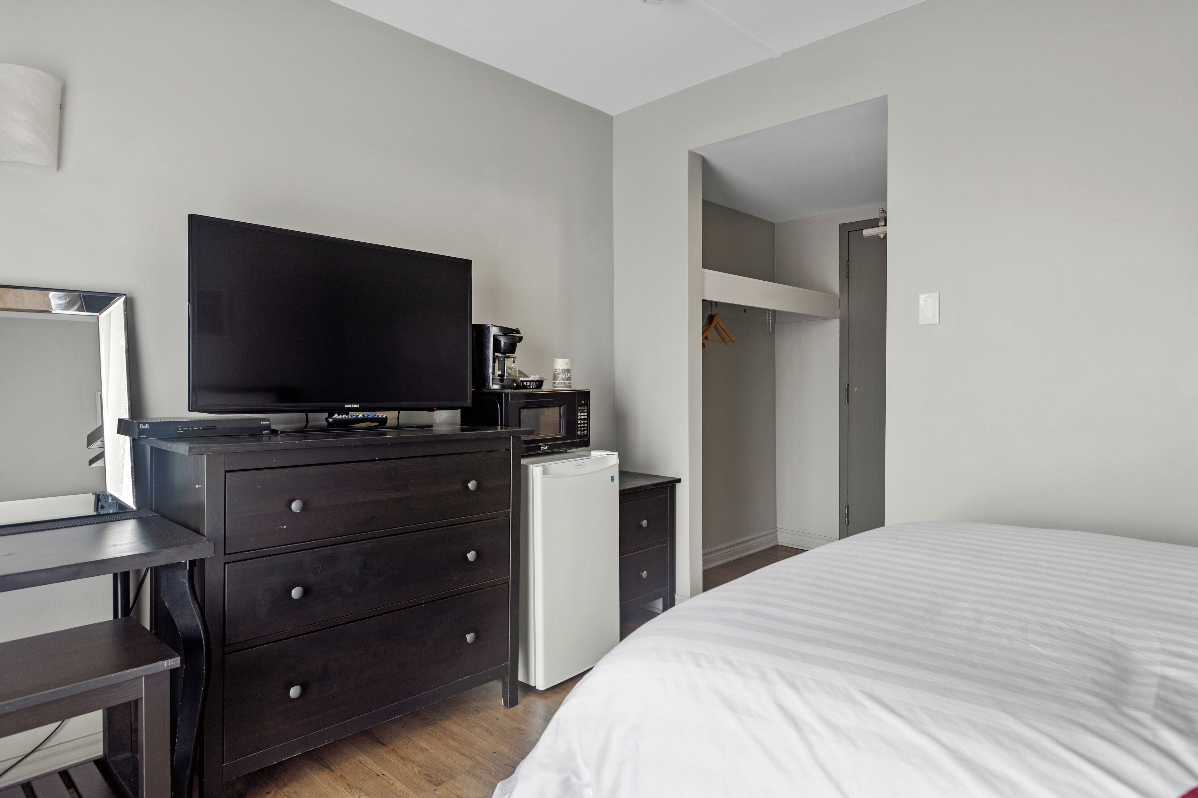 A bedroom with a bed, a dresser, a television, a microwave, and a small refrigerator.