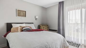 A neatly made bed with a red throw blanket, a wall-mounted light, and a sign with three words.