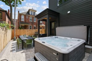 A backyard with a hot tub, a wooden deck, and a patio table with chairs. - Rooftop Deck, Hot Tub, Speakeasy, Columbus Luxury (Columbus)