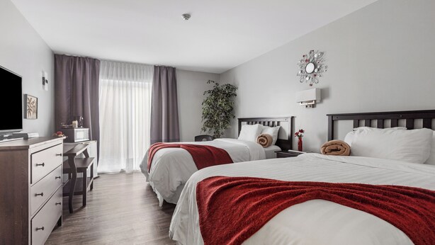Hotelkamer met twee bedden, een bureau, een televisie en een groot raam met gordijnen.