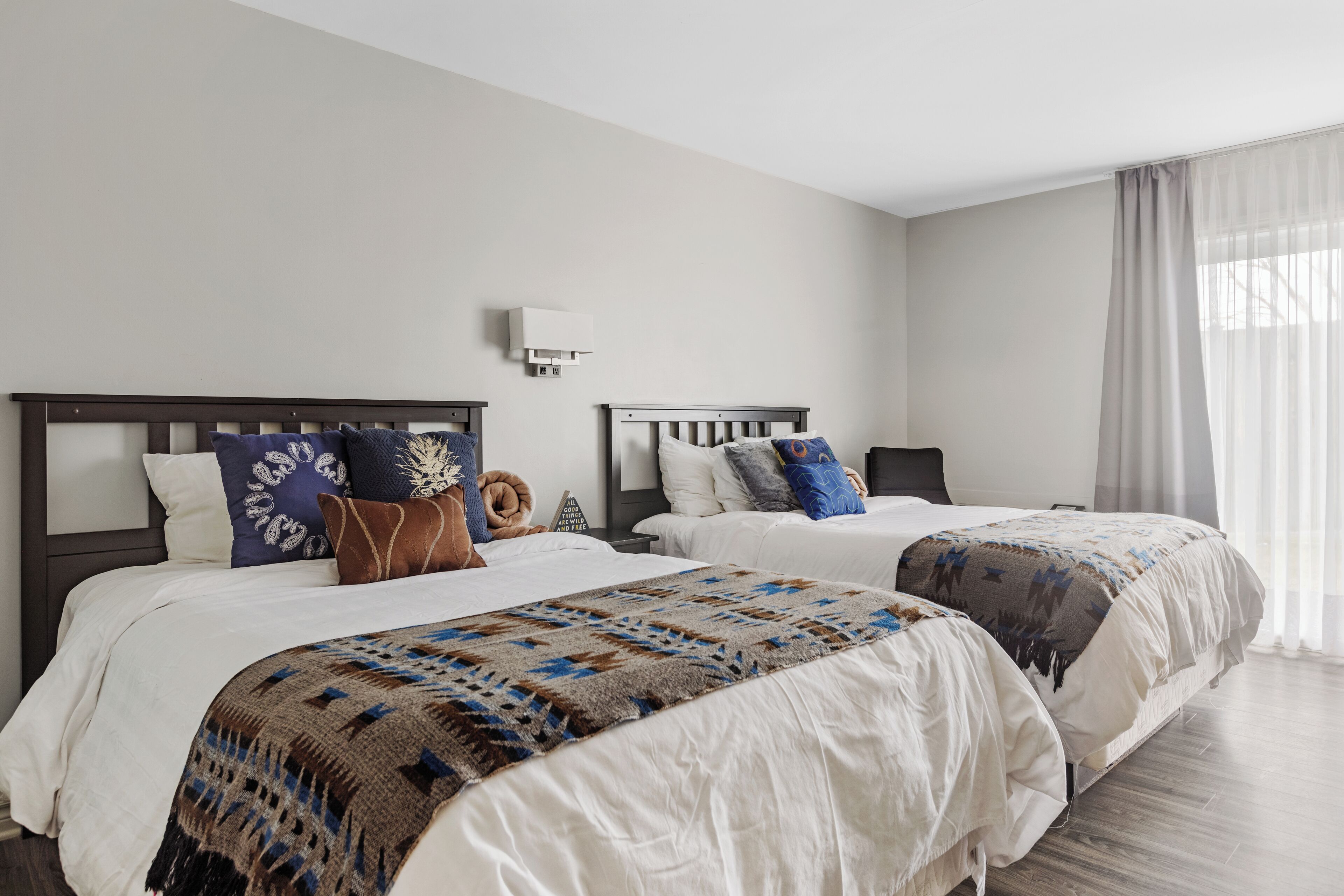 A hotel room with two beds, white bedding, and a patterned throw blanket.