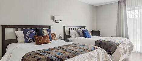 A hotel room with two beds, white bedding, and a patterned throw blanket.