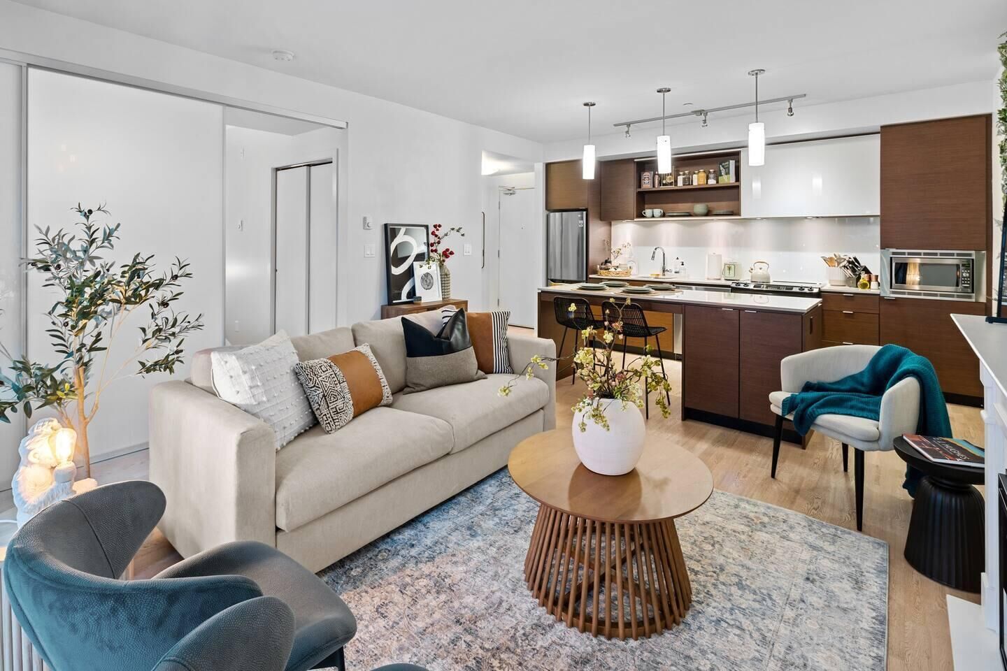 Un salon moderne avec un canapé, une table basse et des fauteuils. Il y a également un coin cuisine équipé de placards et d’un four à micro-ondes.