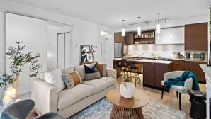 A modern living room with a sofa, coffee table, and chairs. There is a kitchen area with cabinets and a microwave. - Luxe King Bed and Private BBQ Terrace (Victoria North)