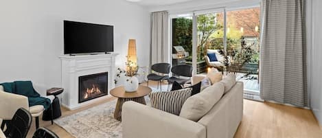 A modern living room with a fireplace, a flat-screen TV, and a large window with curtains.