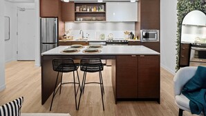 A modern kitchen with a central island, bar stools, a refrigerator, microwave, and a stove. - Luxe King Bed and Private BBQ Terrace (Victoria North)