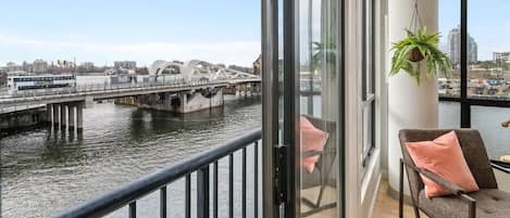 Un balcon offrant une vue sur une rivière, un pont et des bâtiments situés de l’autre côté.