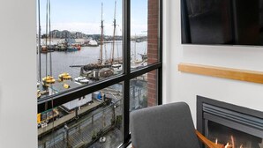 A room with a large window overlooking a harbor, a fireplace, and a mounted television. - Waterfront Stay with Balcony and BBQ (Victoria Central British Columbia Provincial Government)