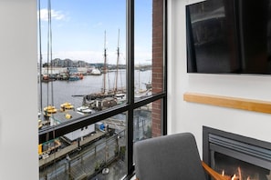 A room with a large window overlooking a harbor, a fireplace, and a mounted television. - Waterfront Stay with Balcony and BBQ (Victoria Central British Columbia Provincial Government)