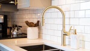 A kitchen with a gold faucet, white tiles, and a black sink. - Waterfront Stay with Balcony and BBQ (Victoria Central British Columbia Provincial Government)