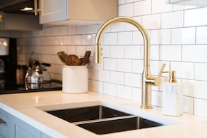A kitchen with a gold faucet, white tiles, and a black sink. - Waterfront Stay with Balcony and BBQ (Victoria Central British Columbia Provincial Government)