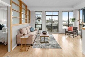 A modern living room with a sofa, a coffee table, and a chair. There is a large window with a view of the city. - Waterfront Stay with Balcony and BBQ (Victoria Central British Columbia Provincial Government)