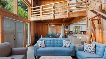 Un vaste espace de vie avec un canapé bleu, un escalier en bois et une cuisine en arrière-plan.