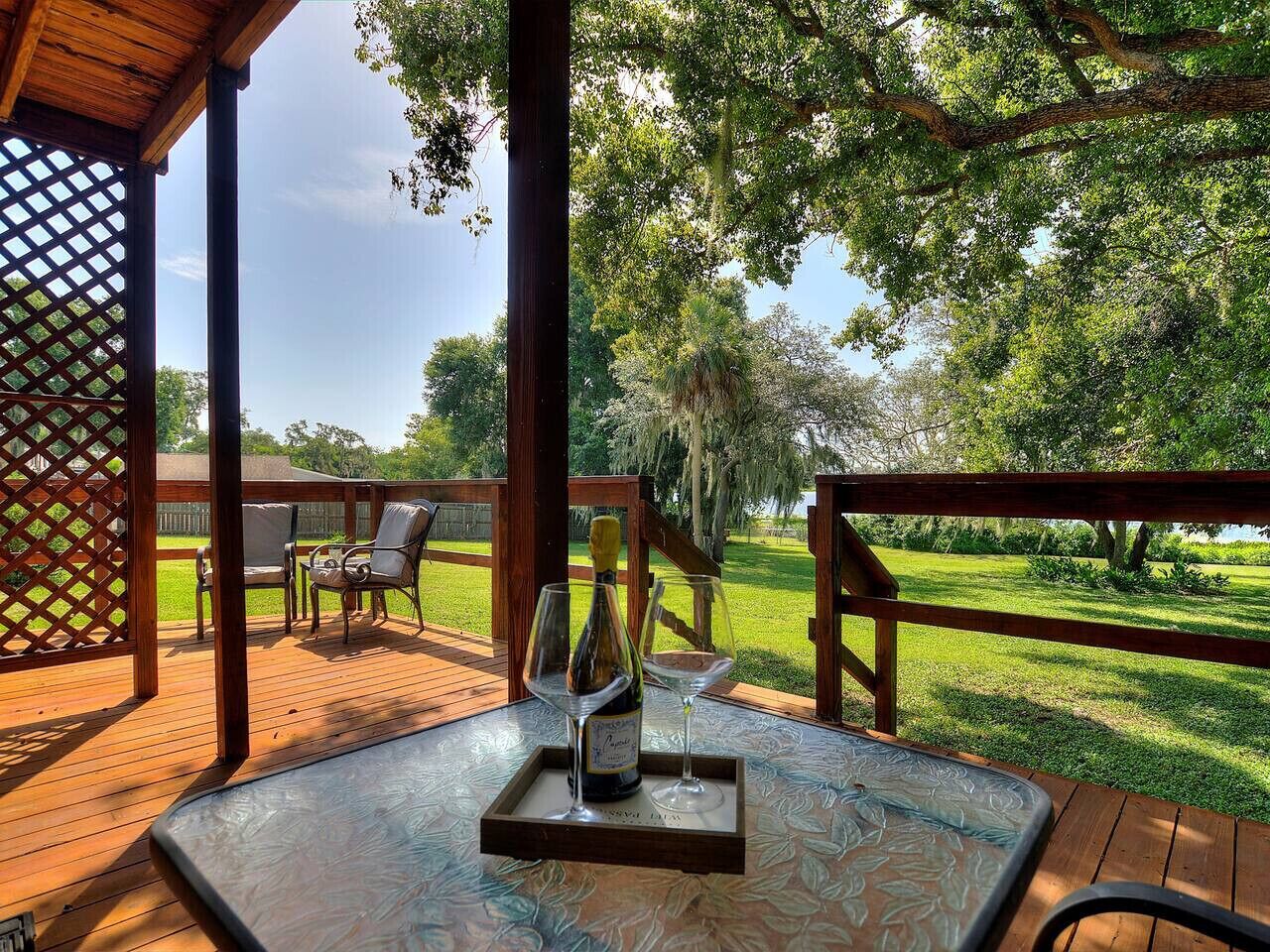 Une terrasse extérieure en bois, avec une table et des chaises, une bouteille de vin et un verre.