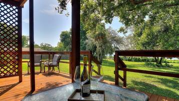 Une terrasse extérieure en bois, avec une table et des chaises, une bouteille de vin et un verre.