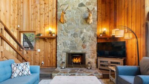 Una sala de estar acogedora con chimenea de piedra, paredes de madera y una televisión.