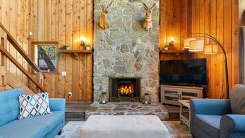 Un salon chaleureux avec une cheminée en pierre, des murs en bois et un téléviseur.