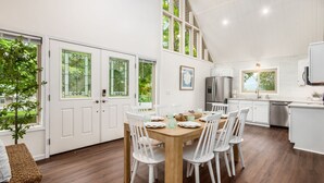 A modern kitchen with white cabinets, a stainless steel refrigerator, and a dining area with a wooden table and white chairs.