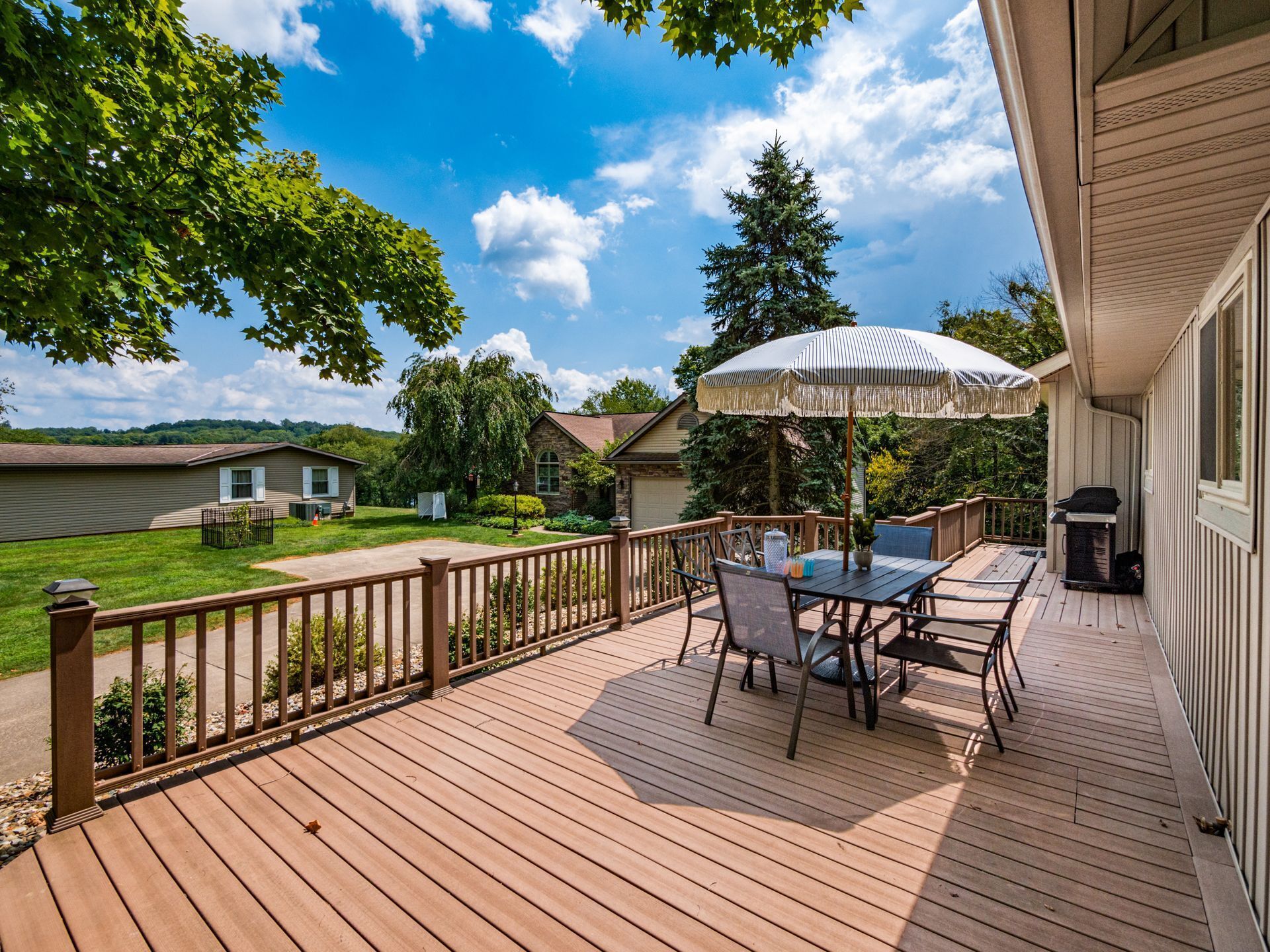 Un terrazzo in legno con tavolo e sedie, un barbecue e un grande ombrellone.