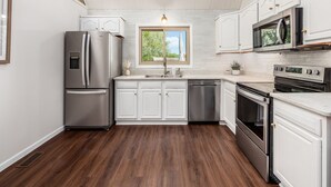 A modern kitchen with white cabinetry, stainless steel appliances, and a wooden floor.