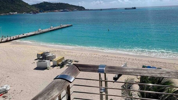 A beach with a wooden deck, a pier extending into the sea, and a clear sky.