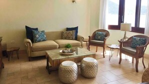 A living room with a beige sofa, two armchairs, a coffee table, and two decorative stools.