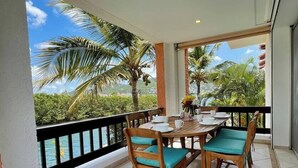 A balcony with a wooden table and chairs, a view of the ocean and palm trees, and a tiled floor. - Simpson bay 3bdr / 3,5 bath with pools - GENERATOR (Simpson Bay)