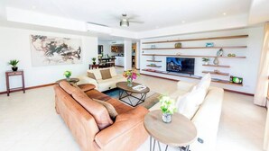 A spacious living room with a large sofa, a coffee table, and a TV. There are shelves with decorative items and a ceiling fan. - Simpson bay 3bdr / 3,5 bath with pools - GENERATOR (Simpson Bay)