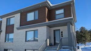 Un immeuble résidentiel moderne à plusieurs étages, doté d’une façade en briques, de grandes fenêtres et d’un porche avant couvert.