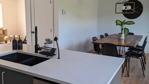 Une cuisine moderne dotée d’un îlot central, d’un coin repas avec une table et des chaises en bois, et d’un luminaire suspendu.