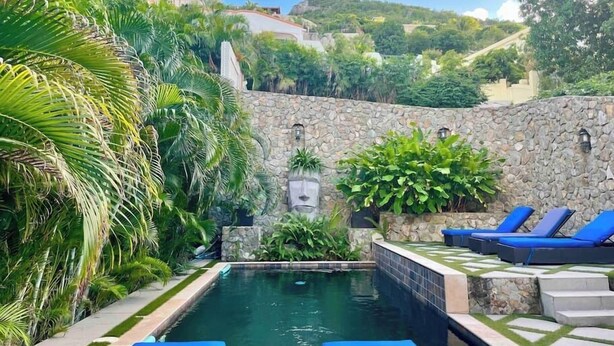A pool area with a stone wall, palm trees, and lounge chairs. - 1 bedroom with pool in Simpson Bay - GENERATOR (1-3B) (Simpson Bay)
