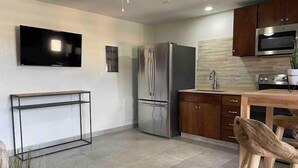 A modern kitchen with a built-in oven, microwave, and refrigerator. There is a wooden dining table and chairs, and a TV mounted on the wall. - 1 bedroom with pool in Simpson Bay - GENERATOR (1-3B) (Simpson Bay)