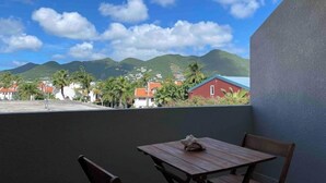 A balcony with a table and chairs, overlooking a town with houses and mountains in the background. - 1 bedroom with pool in Simpson Bay - GENERATOR (1-3B) (Simpson Bay)