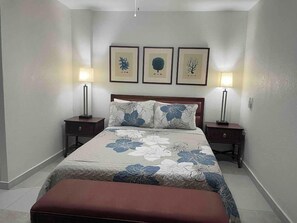 Une chambre à coucher avec un grand lit, deux tables de chevet, un banc et trois tableaux encadrés accrochés au mur.